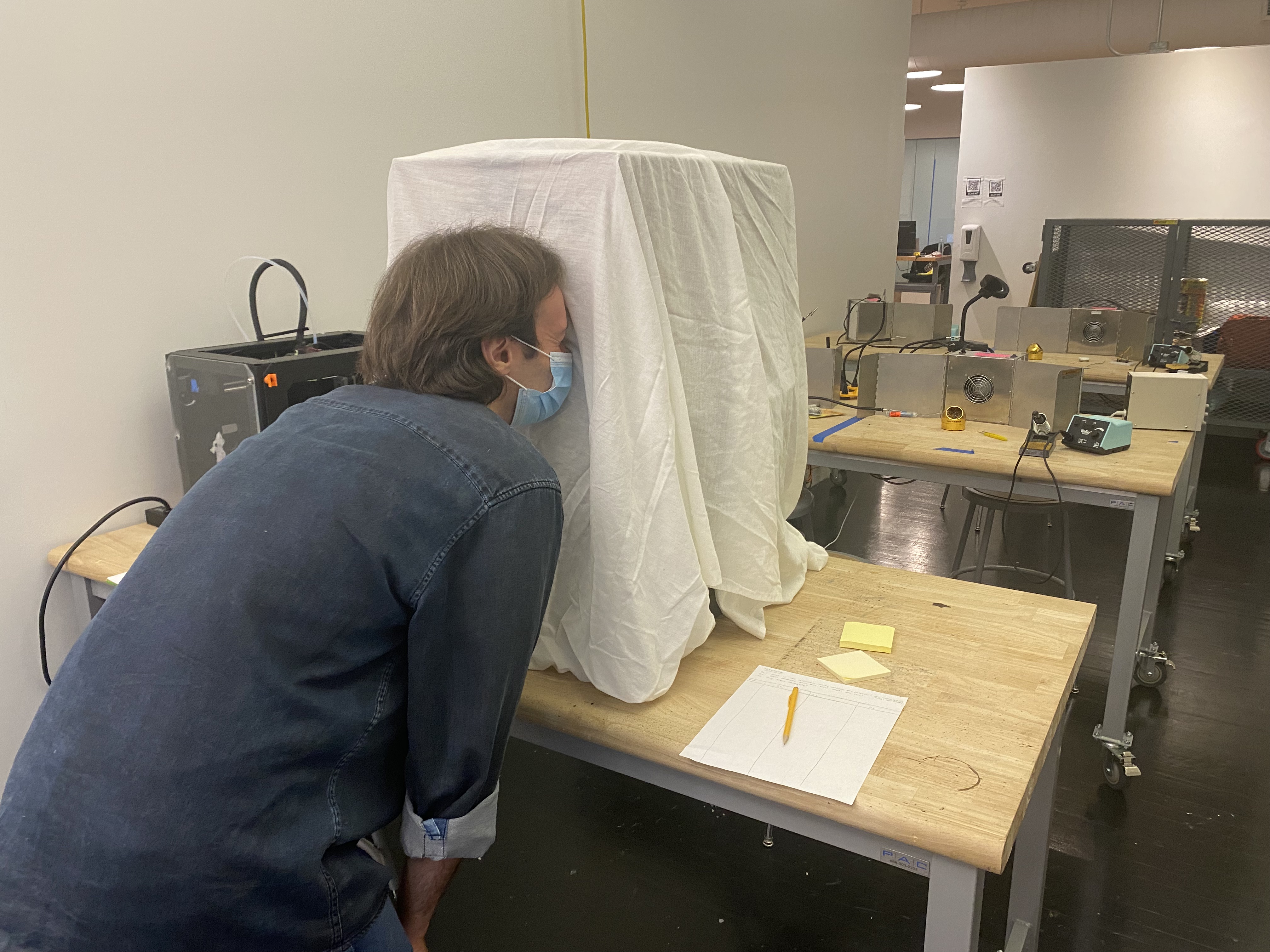 Person looking into a peephole on a box covered with a white sheet.